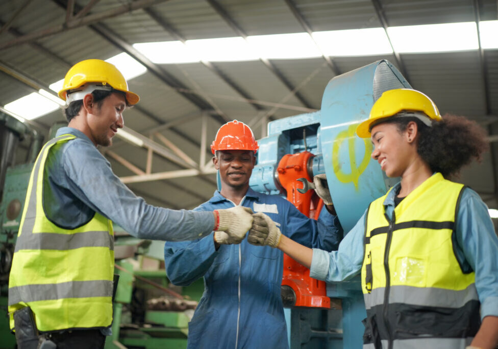 Team maintenance engineers men and women inspect relay protection system with laptop comp. They work a heavy industry manufacturing factory.
